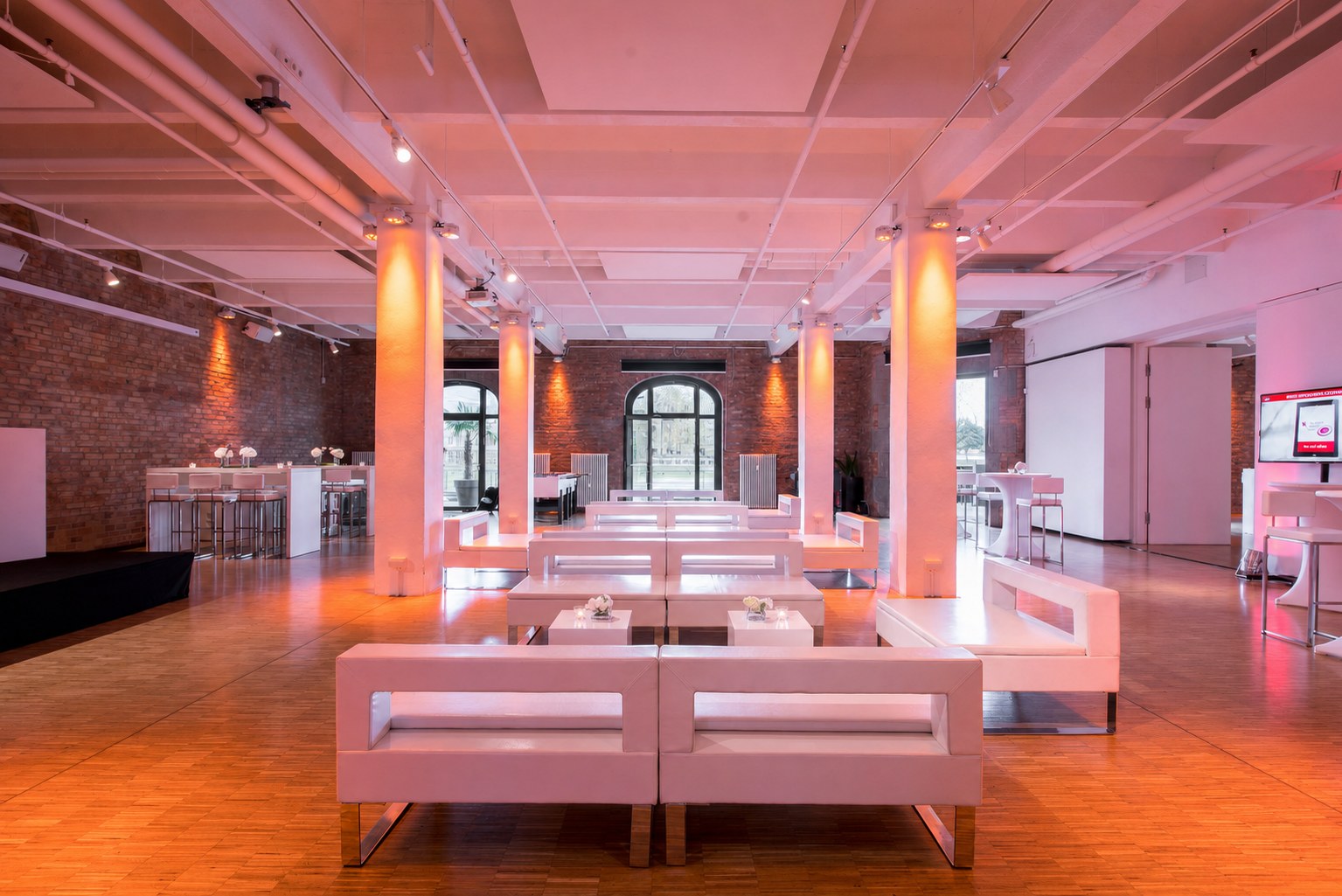 030 Eventloft mit weißer Lounge-Bestuhlung zwischen Säulen und Backsteinwänden