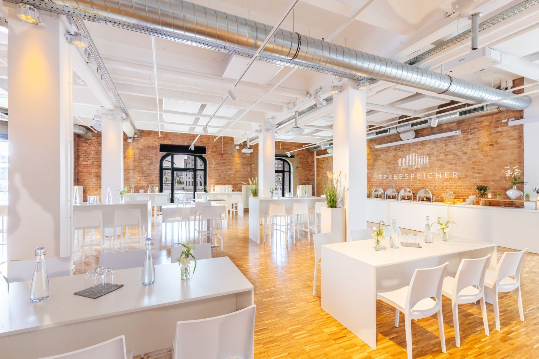 Saal mit Stehtischen, Tafeln und Buffet vor Backsteinwand mit Spreespeicher-Logo
