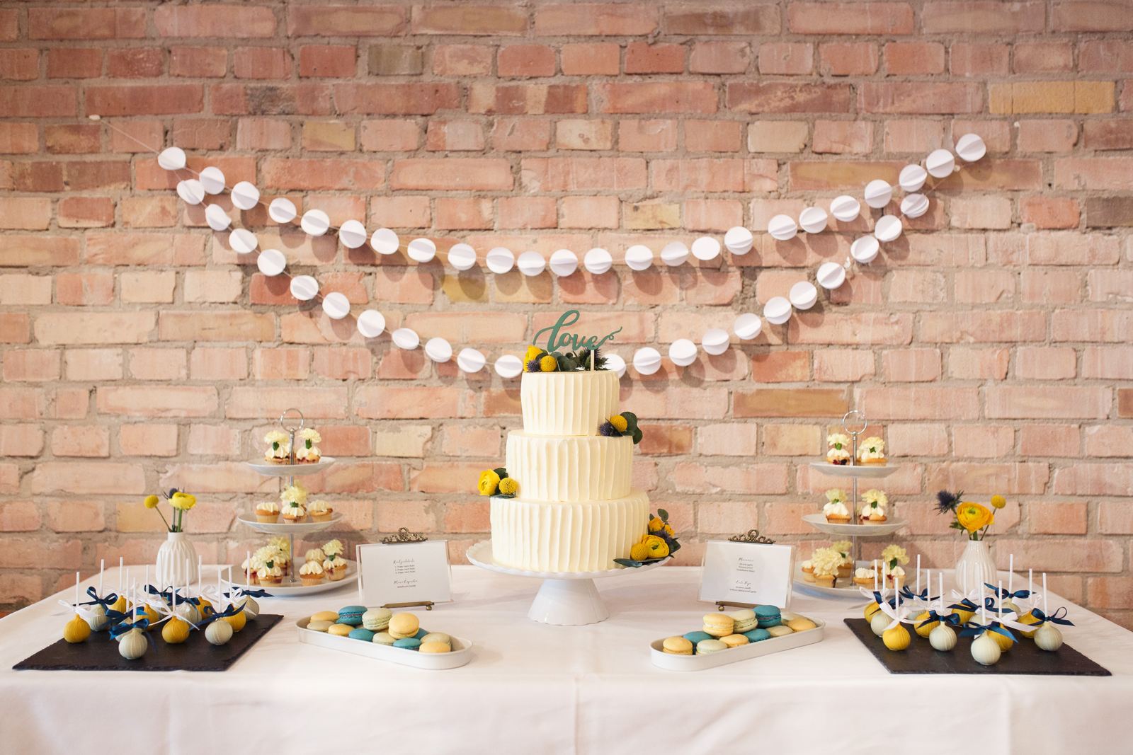 Hochzeitstorte und Dessertbuffet vor einer Backsteinwand